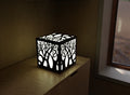 300mm metal cube lamp featuring a enchanted forest cut-out pattern, white plexiglass panels, and a textured black finish.