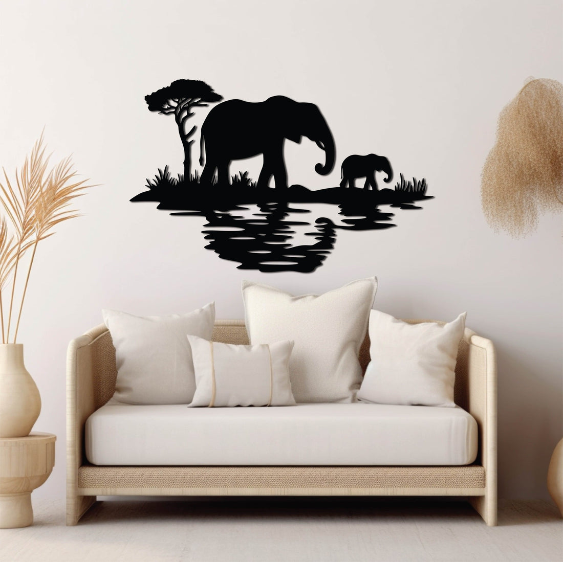 A black metal wall art design depicting an adult elephant and a calf standing near the edge of a reflective water body, accompanied by a solitary tree in the background.