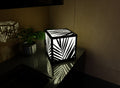 300mm metal cube lamp featuring a palm shadow grid cut-out pattern, white plexiglass panels, and a textured black finish.